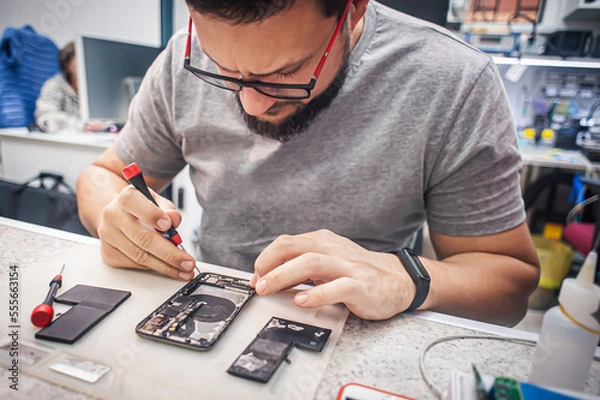 Obraz Workplace top view, close-up. Repairman disassembles smartphone with screwdriver in an electronics repair shop.