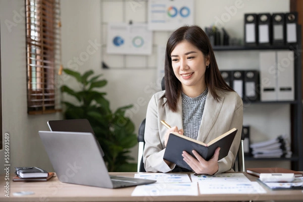 Fototapeta Asian businesswoman secretary sitting happily working on laptop Take notes attentively and smile happily doing the assignments.