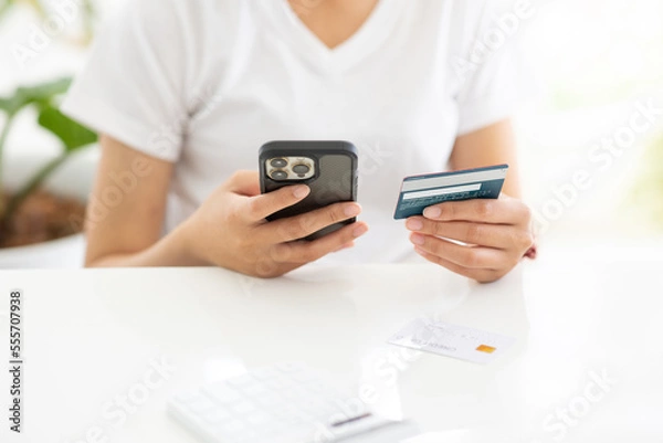 Fototapeta Close up shot of female hand holding credit card and using smartphone for online shopping