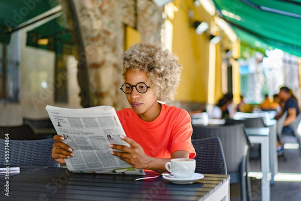 Fototapeta Woman drinking coffee and reading newspaper at cafe. Leisure and news concept