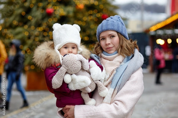 Fototapeta Mother and daughter are walking around the city on Christmas and New Year holidays. Portrait of happy mother and daughter having fun in the street