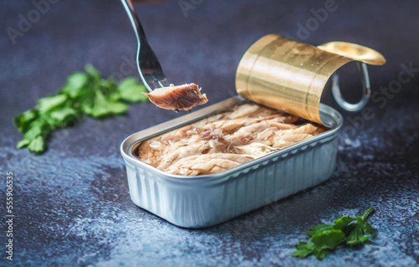 Fototapeta Fork pricking canned mackerel on a dark blue table with parsley. Ready for eat.