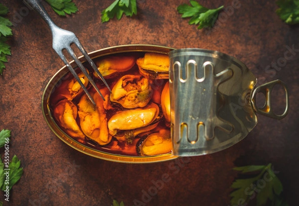 Fototapeta Canned pickled mussels open on a dark brown table with a fork and parsley. Ready for eat. 