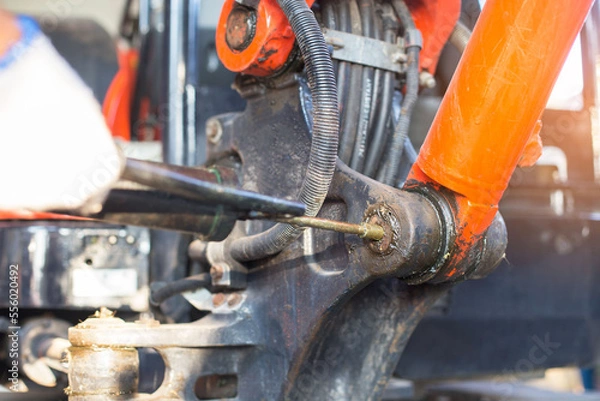 Fototapeta hand of a workman greasing the grease nipple of a hydraulic cylinder the backhoe. Routine Repair Maintenance. the backhoe