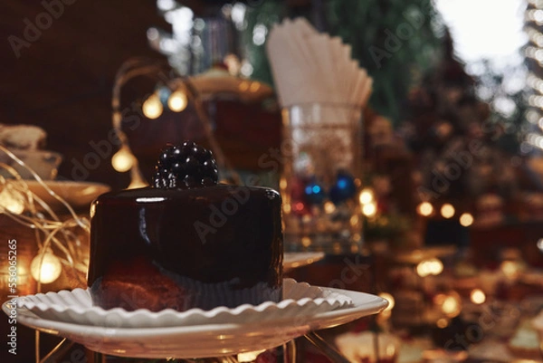 Fototapeta Pastel de chocolate con fondo de adornos navideños, luces cálidas y postres variados