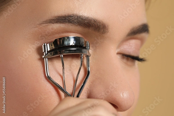 Obraz Woman using eyelash curler on beige background, closeup