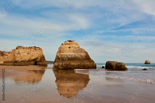 Fototapeta Symmetrical reflection of the limestone rocks in the water of low tide. Praia dos Tres Castelos, Portimao