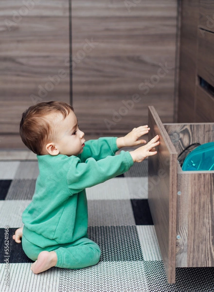 Fototapeta Little boy open the kitchen drawers to play with kitchenware inside. Baby exploring kitchen objects.