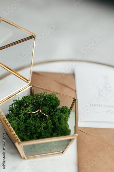 Fototapeta The concept of love and relationships. Wedding invitation. Gold rings in a gold casket on a marble table. Craft envelopes with invitations. Close-up.
