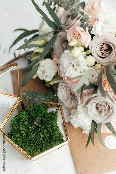 Fototapeta The concept of love and relationships. Wedding invitation. Gold rings in the moss with a gold casket on a marble table. Bouquet. Close-up.