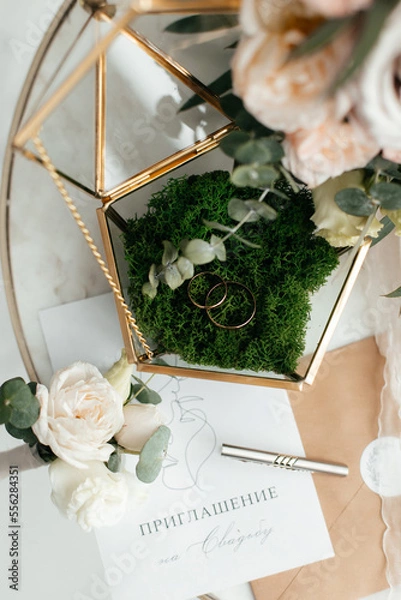 Fototapeta The concept of love and relationships. Wedding invitation. Gold rings in the moss with a gold casket on a marble table. Bouquet. Close-up.
