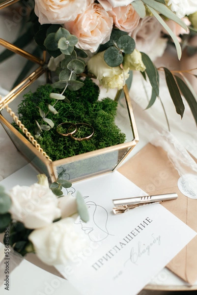 Fototapeta The concept of love and relationships. Wedding invitation. Gold rings in the moss with a gold casket on a marble table. Bouquet. Close-up.
