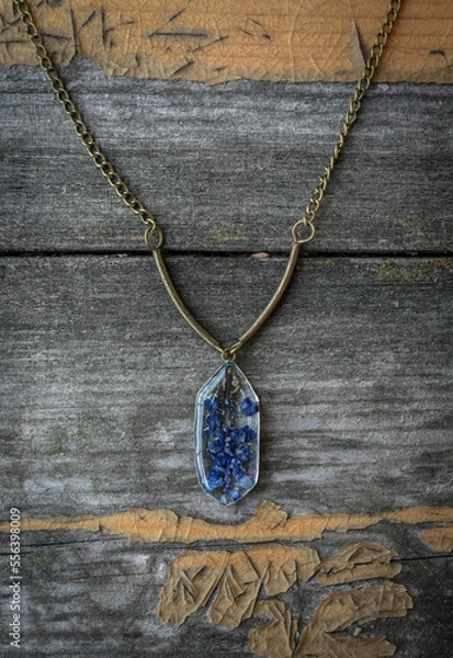 Obraz Close up pendant with small blue flowers concept photo. Craft jewelry. Top view photography with old wooden table on background. High quality picture for wallpaper, travel blog, magazine, article