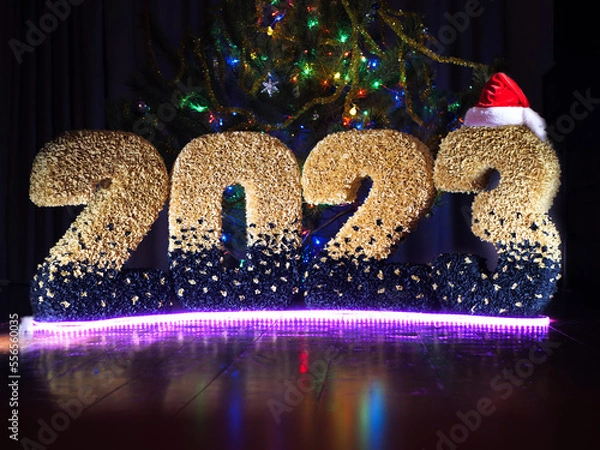 Obraz new year 2023. numbers of the year in yellow color on the background of multi-colored bokeh. New Year's date. New Year's installation against the background of lanterns. numbers on a bokeh background.
