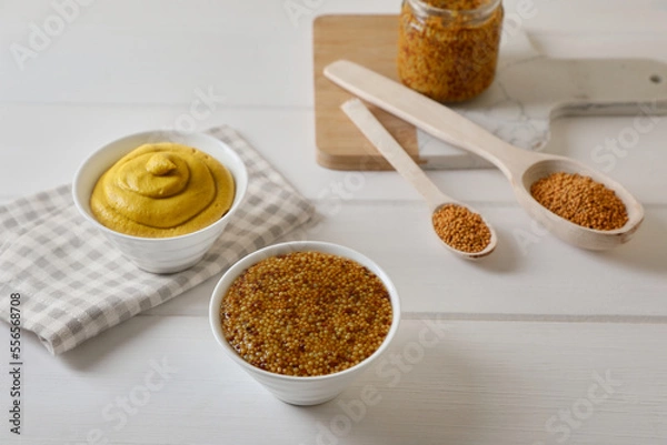 Fototapeta Bowls and spoons of whole grain mustard with seeds on white wooden table