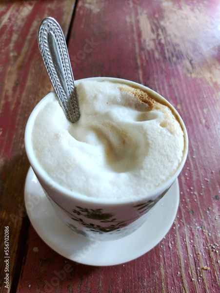 Fototapeta Tasty and creamy cappuccino coffee in a beautiful cup on a raw wood amaranth table. Italian breakfast concept. Close up view.
