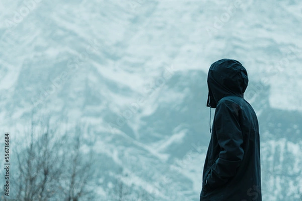 Fototapeta Rear view shot of an Indian male traveler looking at the snow covered mountains during the snowfall at Lahaul Spiti in Himachal Pradesh, India. Man staring at snow mountain in winter.  