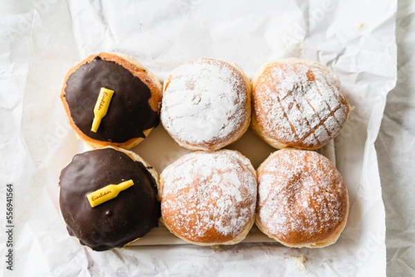 Fototapeta Assorted Krapfen, Berliner doughnuts or Pfannkuchen filled with jam or custard wrapped in white paper fresh from German bakery, traditional fried yeast dough pastry for New Years or carnival party