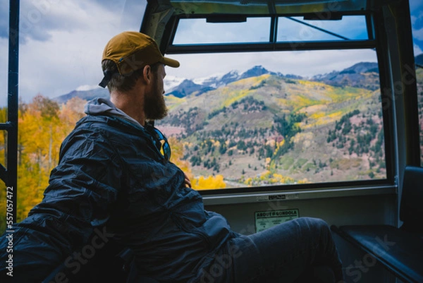 Fototapeta Man riding in a Gondola looking out the window over a scenic landscape of mountains and golden aspens in Telluride, Colorado