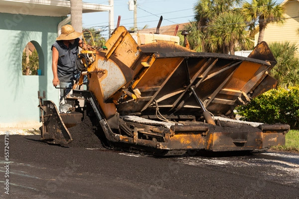 Fototapeta Cocoa Beach, Florida, USA, 2022. Asphalting worker applying tarmac from a asphalt paver machine to resurface a Florida driveway.