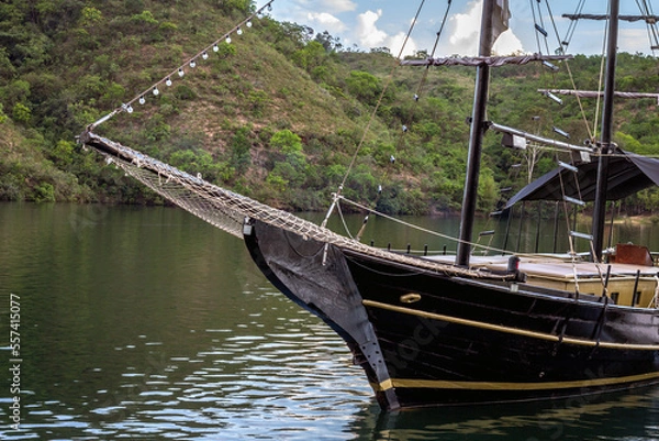 Fototapeta Close up of black boat (schooner) sailing on calm lake with mountains in the background