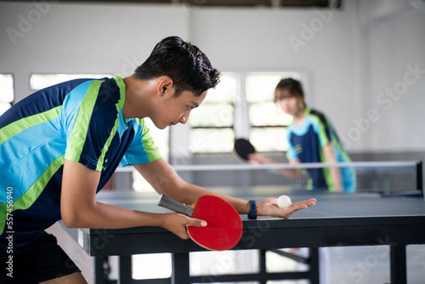 Fototapeta Male athlete carrying a ball and paddle while serving a ping pong game at a ping pong table