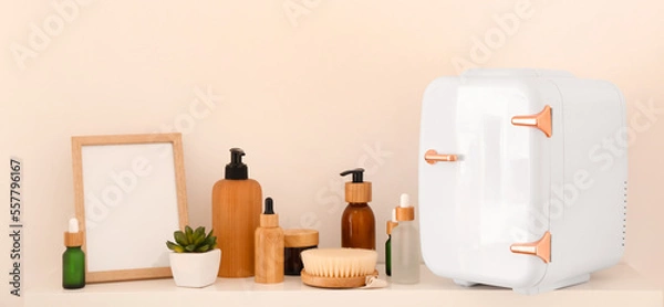Fototapeta Shelf with small refrigerator and cosmetic products near light wall