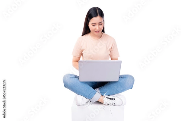 Obraz Happy young asian woman sitting on white chair with legs crossed and using laptop computer on light pink background copy space Full body young smiling happy female wearing t shirt and jeans lifestyle