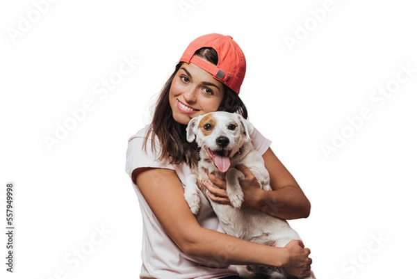 Fototapeta Waist up shot of caucasian young female holds tightly puppy, laughs sincerely, rejoices present from friend, likes devoted animals, wears white shirt, models over transparent background. Friendship.