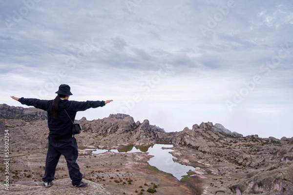 Obraz Latin man with open arms, looking out over the valley, with a lagoon and a valley of rocks in the background.