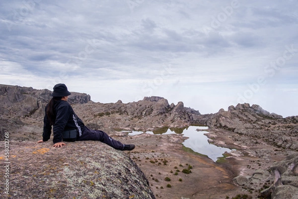 Obraz half-sitting latin man with his arms supporting her, with a lagoon and a valley of rocks in the background.