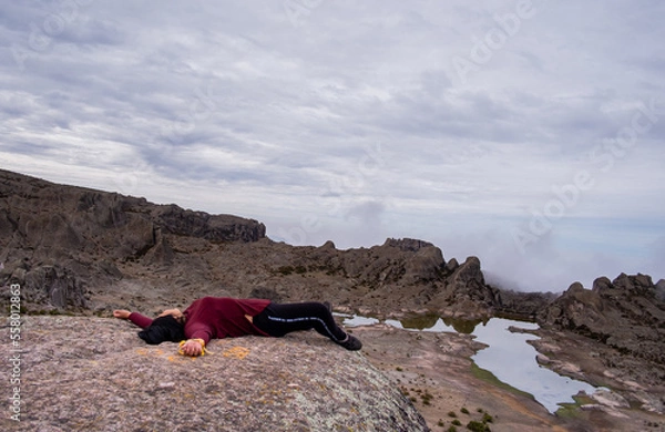 Obraz latina woman lying on a rock, with a lagoon and a valley of rocks in the background