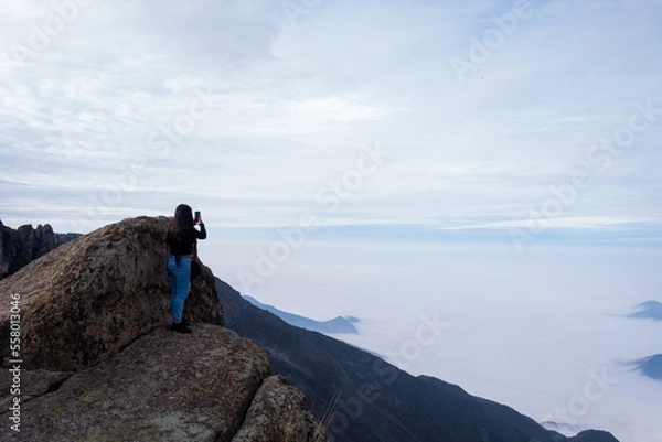 Obraz landscape where a latin woman sees a cushion of clouds, standing on the edge of a cliff in the Peruvian Andes.