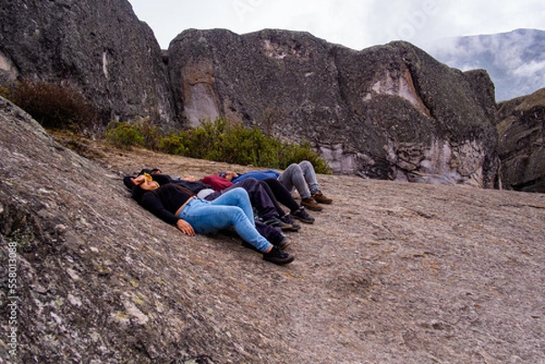 Obraz group of friends lying on a rock, on a plateau in the Peruvian Andes, where there are rocks and fog in the background.