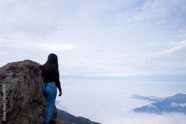 Obraz landscape where a latin woman sees a cushion of clouds, standing on the edge of a cliff in the Peruvian Andes.