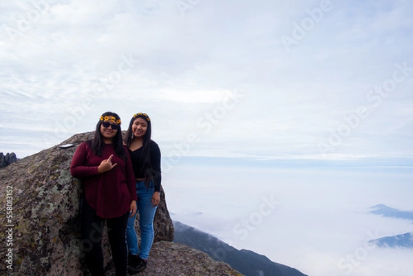 Obraz a lesbian couple taking a picture of themselves, on the edge of a cliff in the Peruvian Andes, to be able to see the cloud bed.
