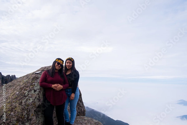 Obraz a lesbian couple taking a picture of themselves, on the edge of a cliff in the Peruvian Andes, to be able to see the cloud bed.