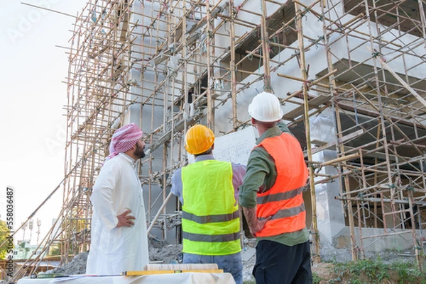 Fototapeta Diverse team of professionals using tablet computers on construction site. Real estate construction project. with civil engineers, architects, Arabic business investors and explorer with theodolite