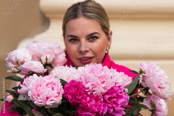 Fototapeta Portrait of caucasian blonde woman in crimson dress with bouquet of pink peonies. Young female holding bunch of flowers.