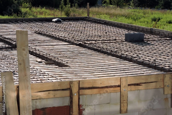 Fototapeta A steel reinforcement for the concrete floor and pillars on the first floor of a house under construction, a wooden formwork, a smoke and ventilation chimney, walls made of aac