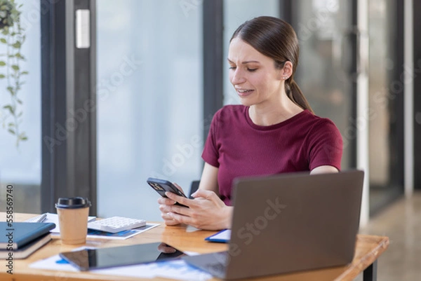 Fototapeta Portrait of Young canada american business woman using a mobile phone and works on a laptop computer in the modern home workplace office