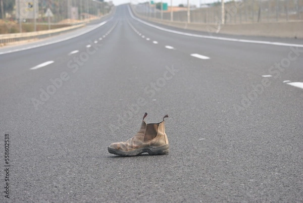 Fototapeta Old boot, useless item, on empty highway. Solitude concept