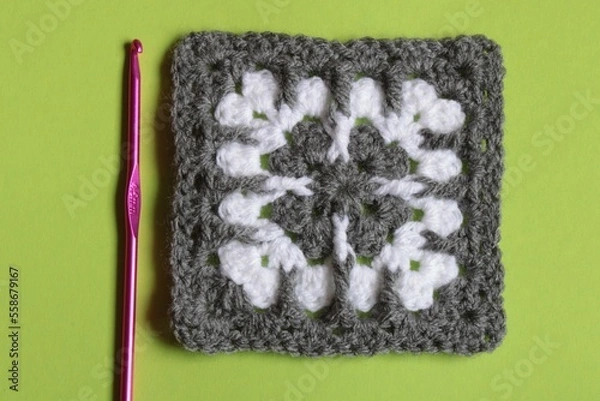 Fototapeta Modern Crochet granny square in grey and white with crochet hook isolated on a plain green background with copy space