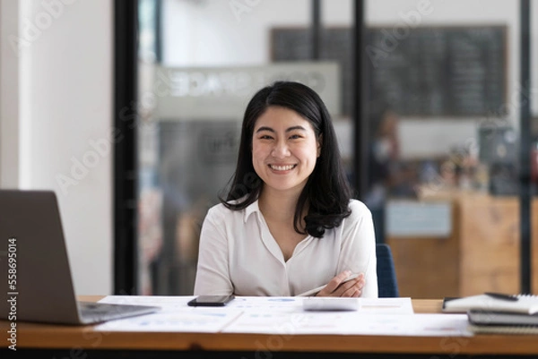 Obraz Charming Asian businesswoman sitting in the office with a digital laptop computer. Excited Asian businesswoman raising hands to congratulate while working in a modern office,