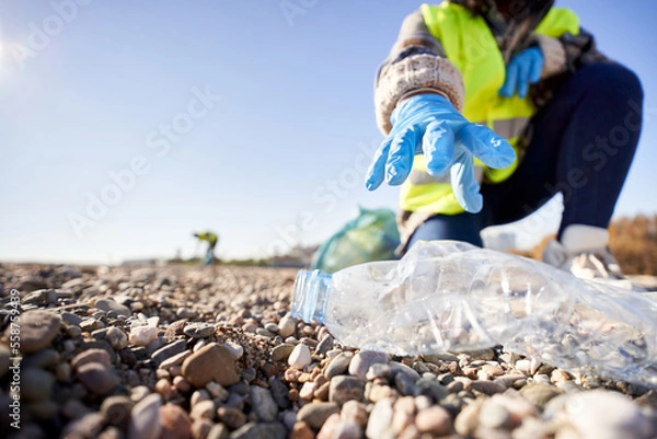 Obraz Group of cleanup volunteers cleaning up waste in nature and holding a garbage bag trash. Close up of activist hand picking up a plastic bottle. Concept of environmental protection.