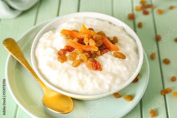 Obraz Bowl with delicious rice pudding, raisins, dried apricot and spoon on green wooden table
