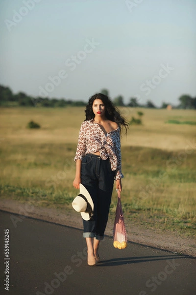 Fototapeta Magnificent volume
curly hair; The dark-haired girl is wearing jeans and a light shirt; a sexy girl walks down the road; red lipstick on the lips;