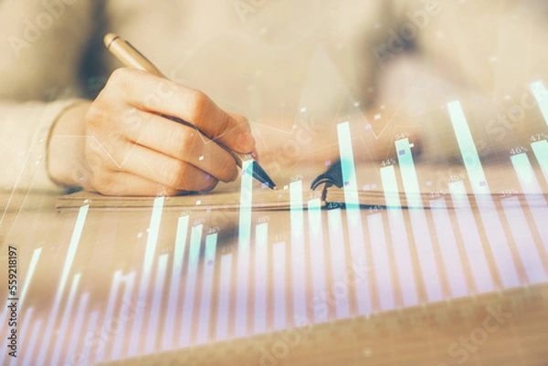 Fototapeta Hands writing information about stock market in notepad. Forex chart holograms in front. Concept of research. Multi exposure
