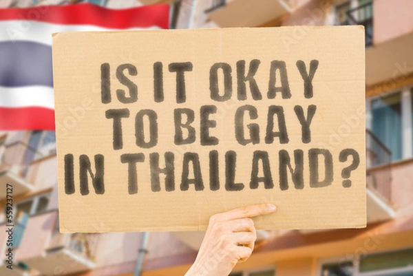 Fototapeta The question " Is it okay to be gay in Thailand? " is on a banner in men's hands with blurred background. Friendly. Passionate. Contact. Date. Dating. Lover. Partner. Boyfriend. Pleasant. Approval
