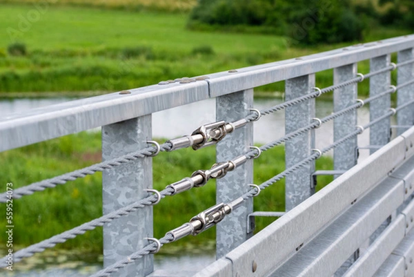 Fototapeta Turnbuckles connecting the safety ropes at the railing on the bridge. Summer.